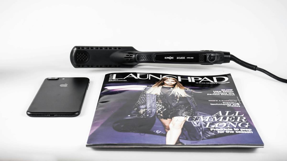 Close-up of digital smoothing irons with illuminated temperature display and ergonomic grip, placed on a marble countertop beside a heat-protectant spray bottle